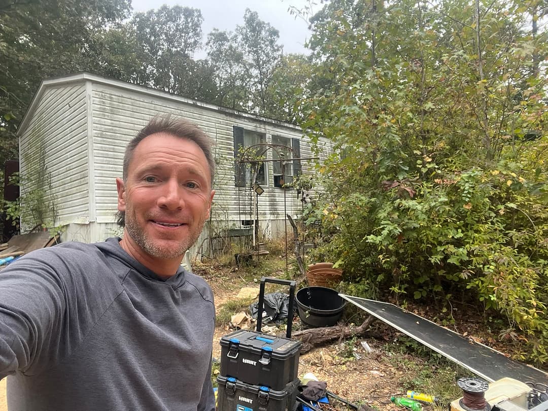 Rusty on a job site in front of a weathered mobile home he is buying as-is